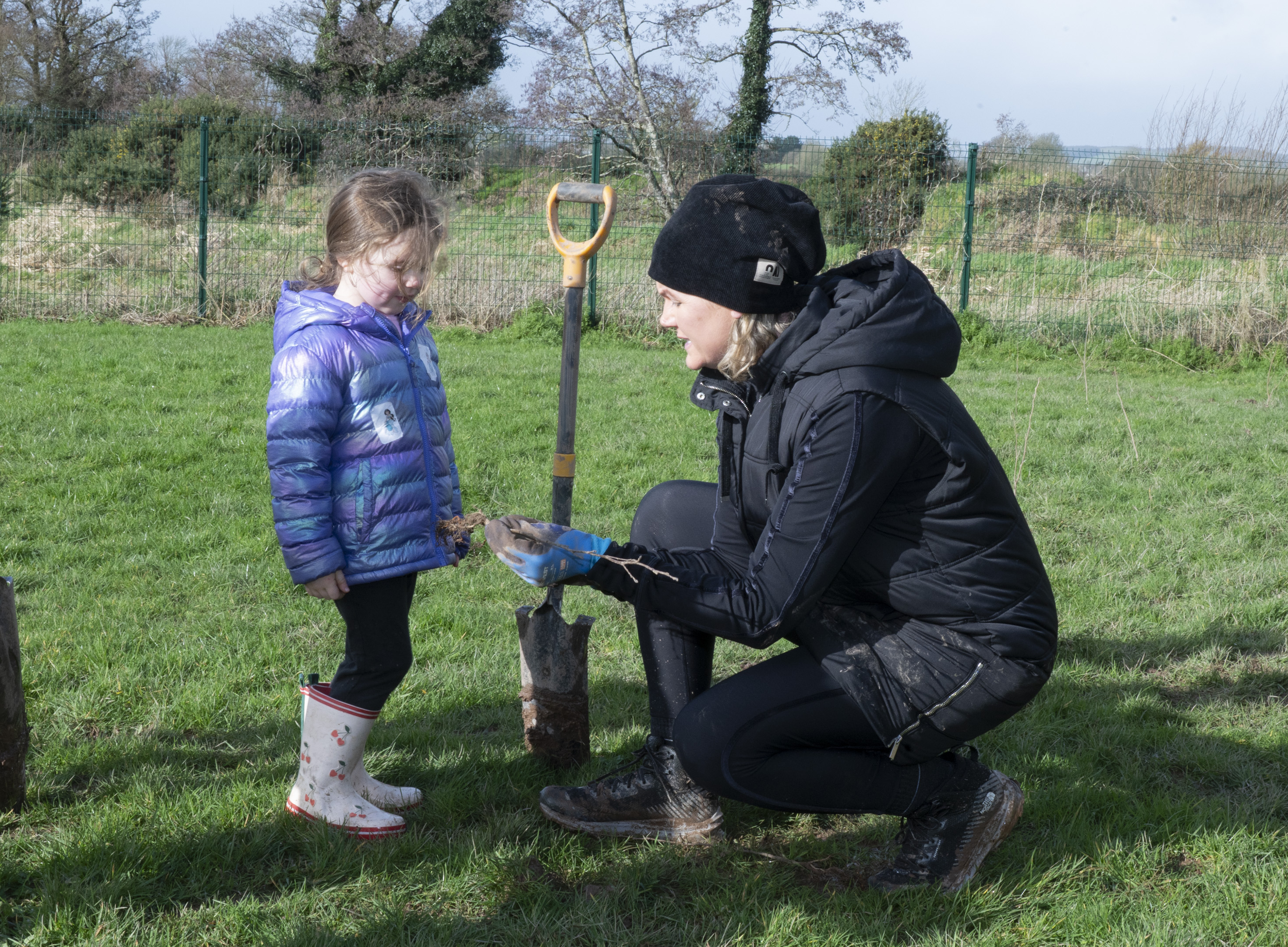 A volunteer explains the planting process to a young participant during the tree planting day at Curraheen Park, highlighting the educational and community engagement aspect of the biodiversity initiative.
